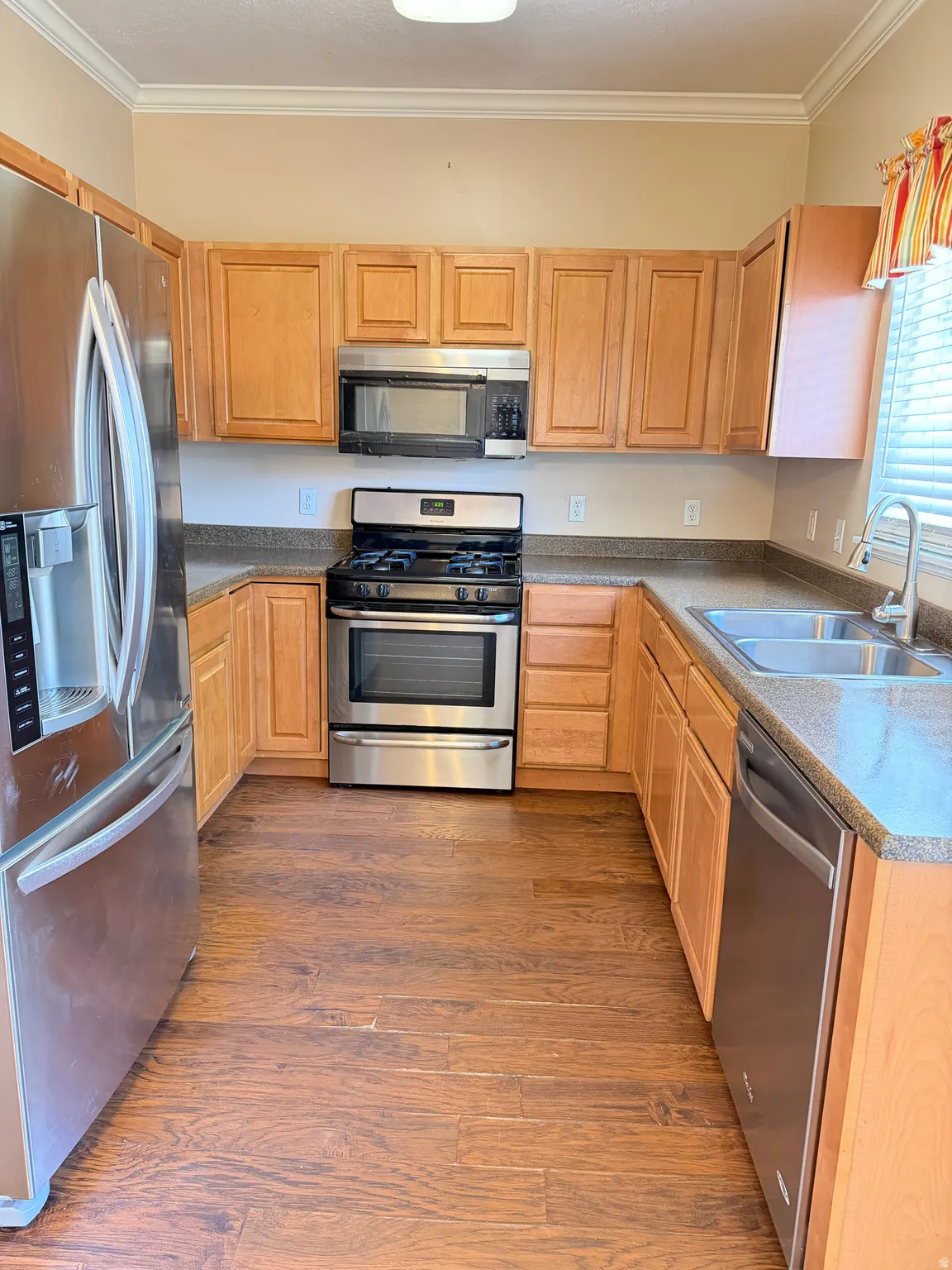 Kitchen featuring stainless steel appliances, light wood finish cabinets, crown molding, and dark wood-style flooring