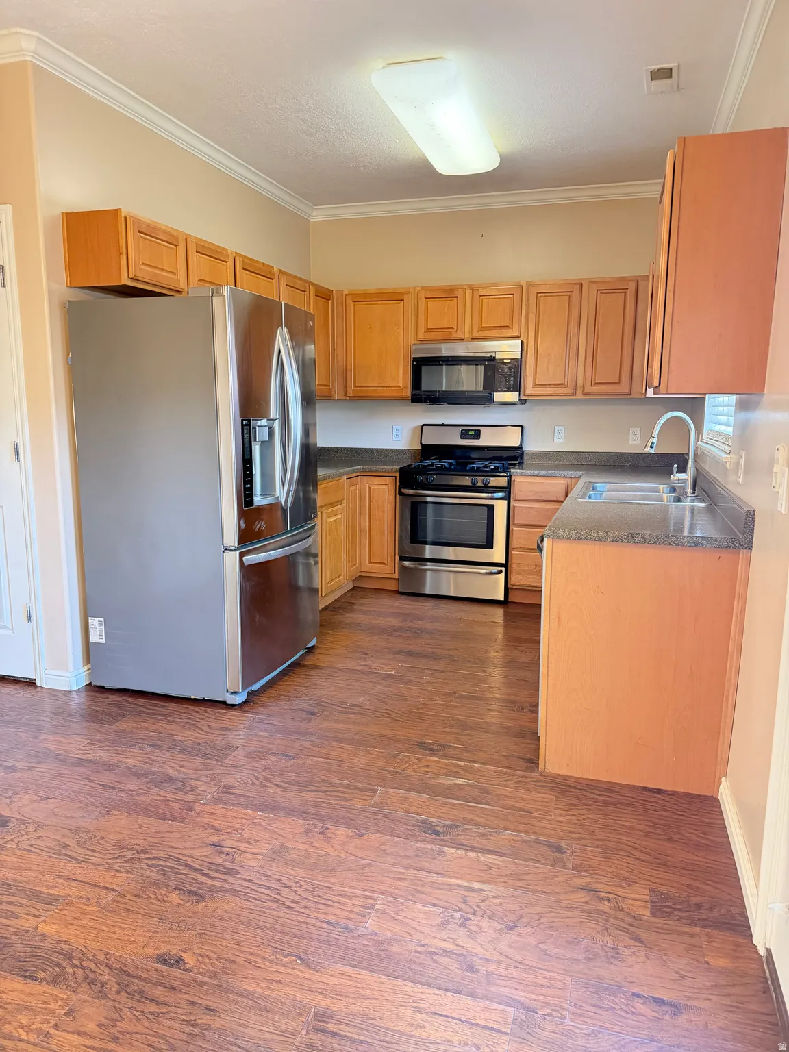 Kitchen featuring stainless steel appliances, crown molding, and dark wood-style flooring