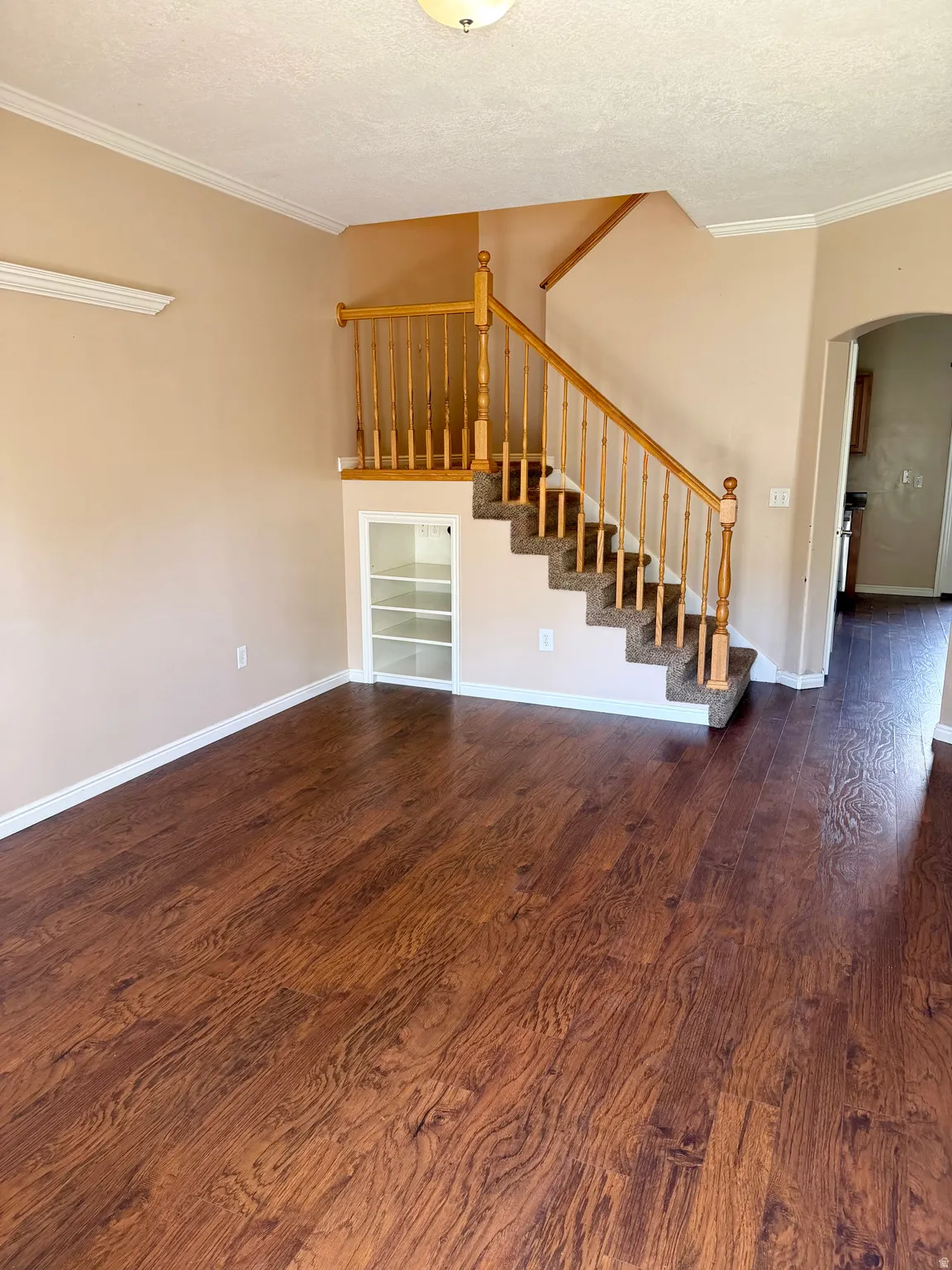 Unfurnished living room with dark wood-style floors, a textured ceiling, arched walkways, and ornamental molding