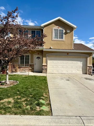 Traditional-style home with stone siding, driveway, stucco siding, an attached garage, and a front yard