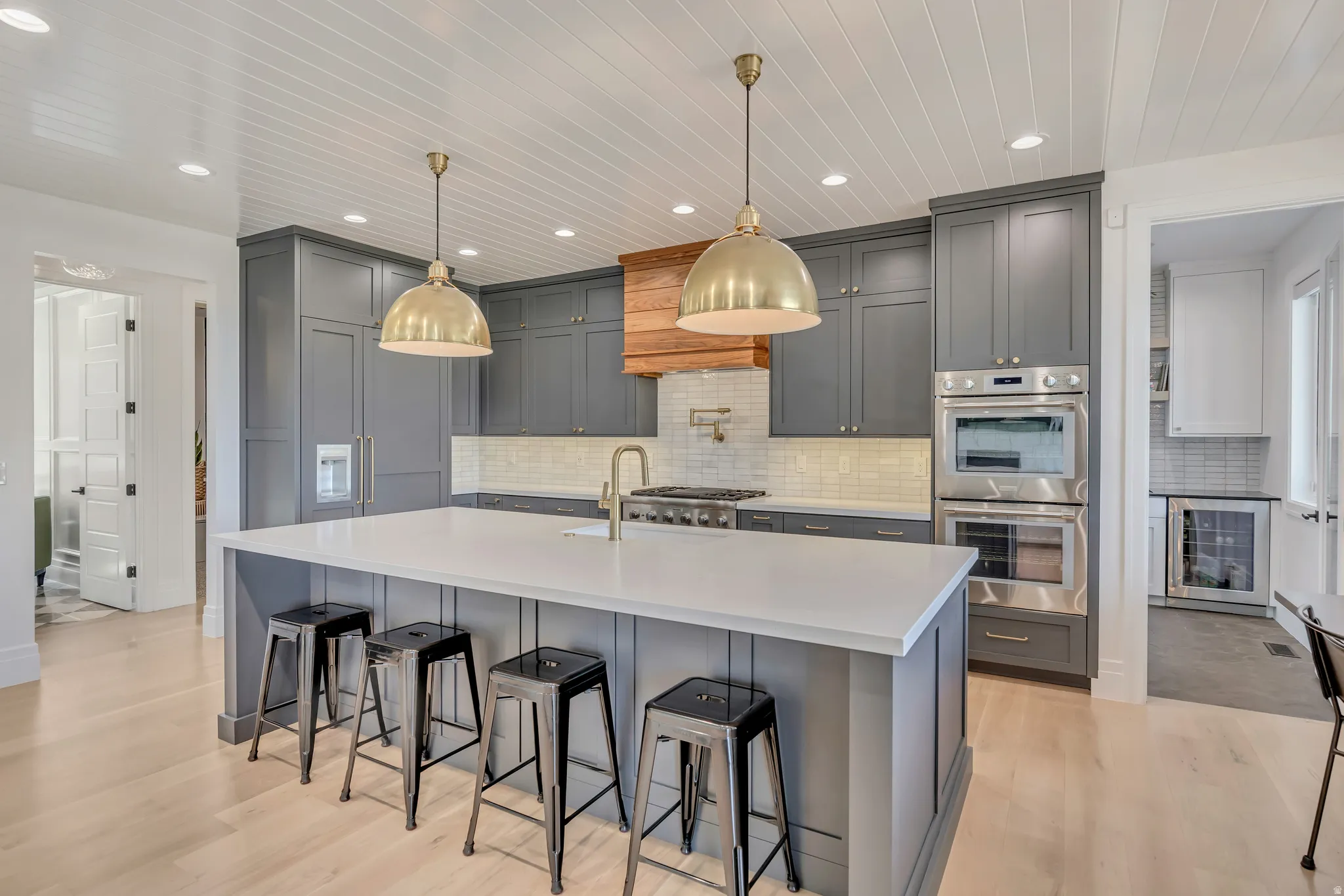 Kitchen with gray cabinets, a breakfast bar area, stainless steel appliances, a large island, and decorative light fixtures