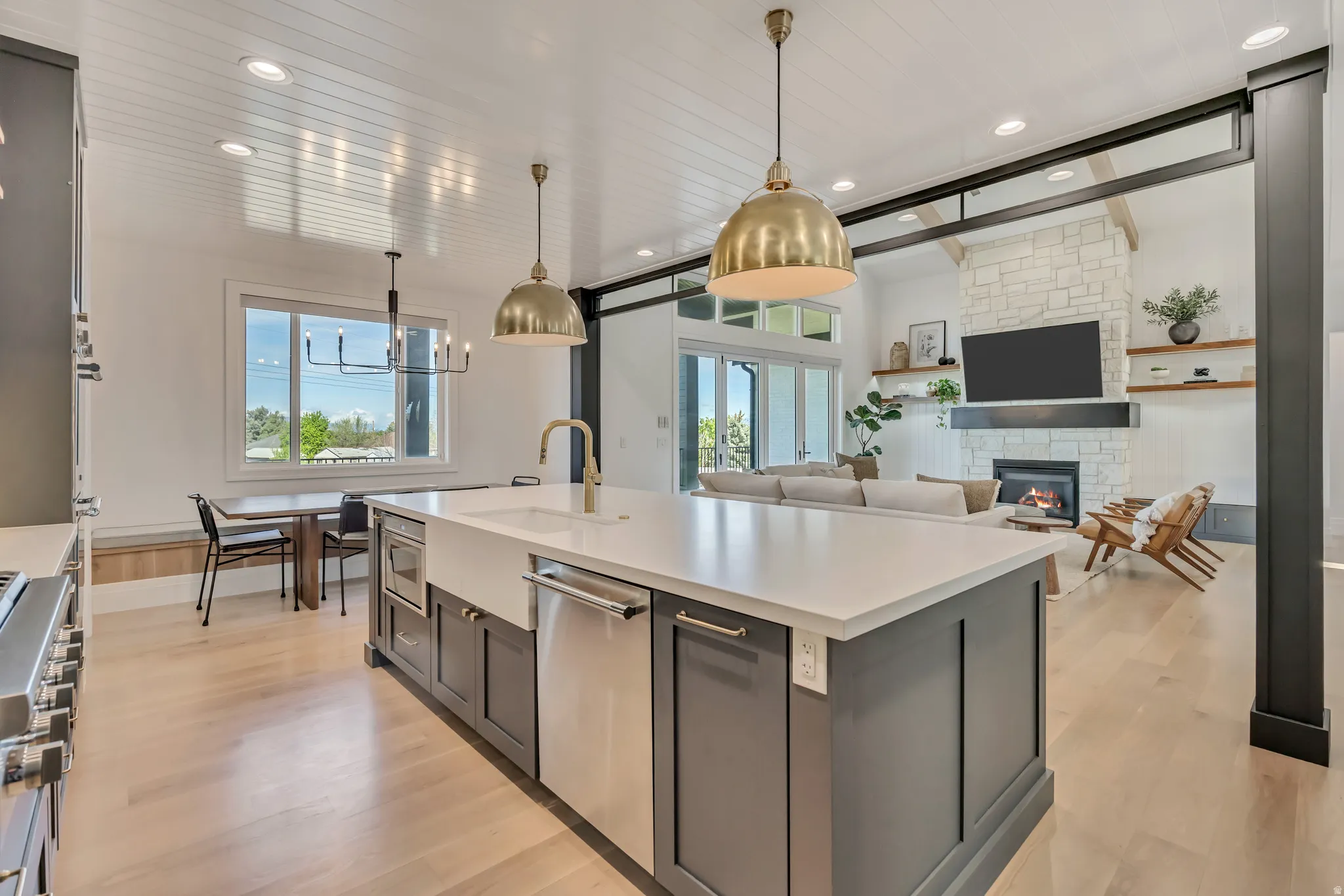 Kitchen featuring light wood-type flooring, open floor plan, hanging light fixtures, stainless steel appliances, and a fireplace