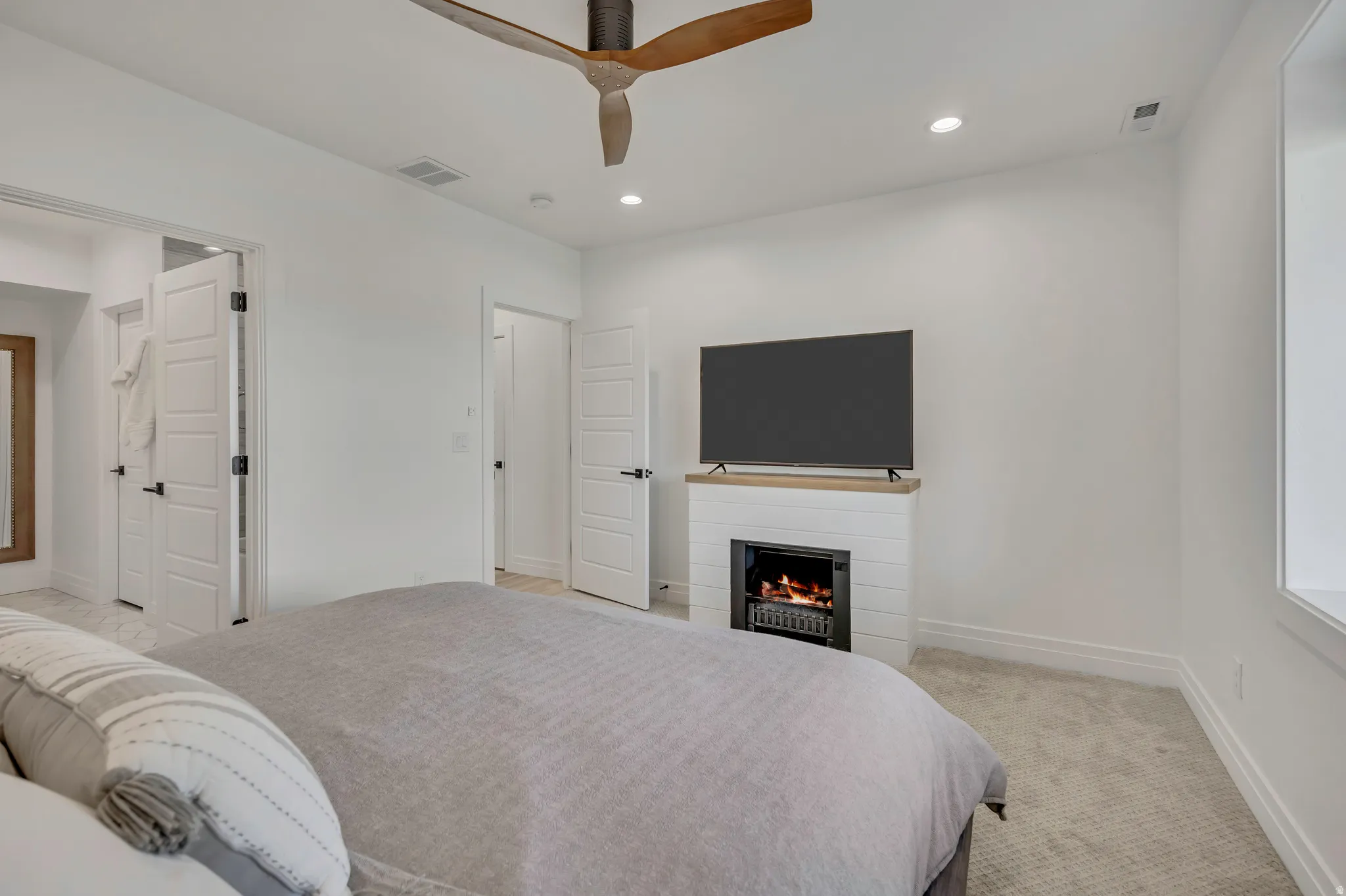 Bedroom with light carpet, recessed lighting, a warm lit fireplace, and ceiling fan