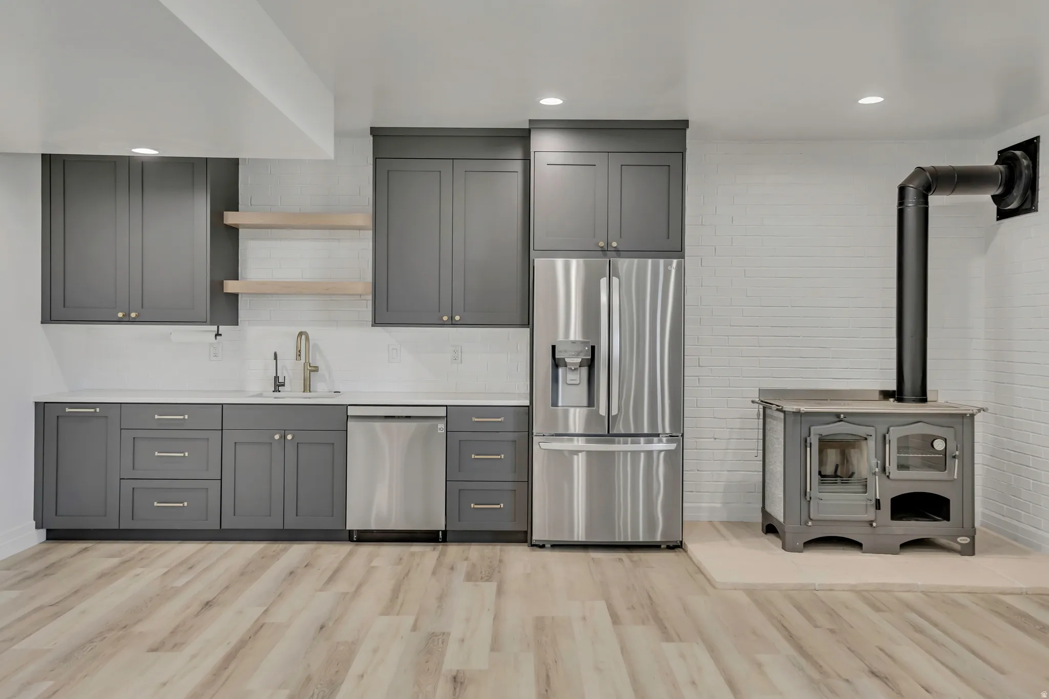 Kitchen with gray cabinets, open shelves, stainless steel appliances, a wood stove, and light wood-type flooring