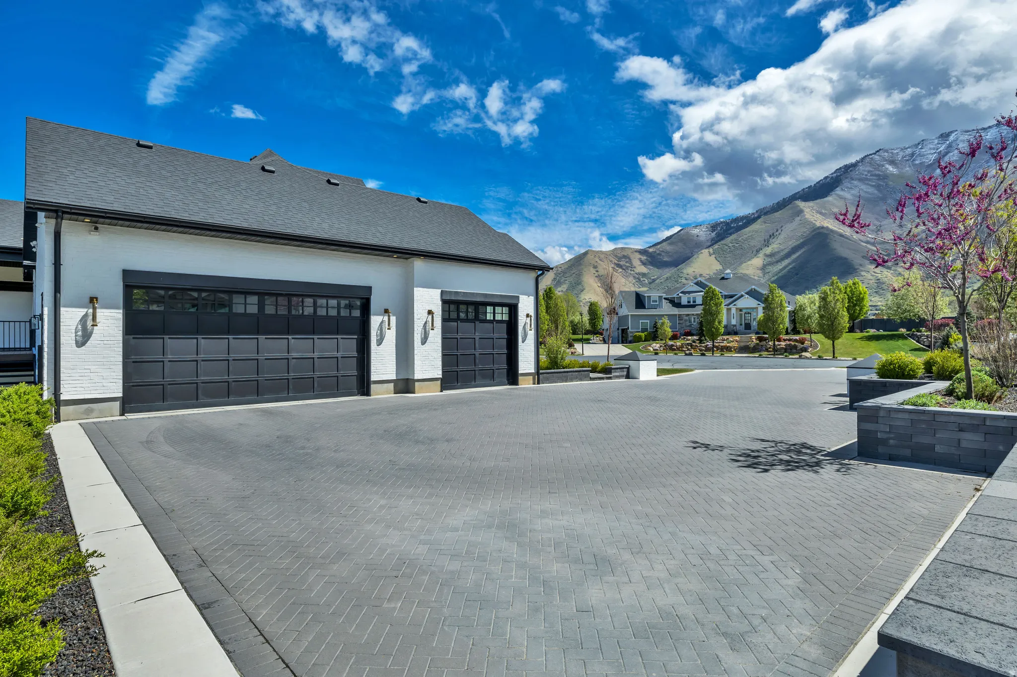 View of side of home with a mountain view, decorative driveway, an attached garage, and a residential view