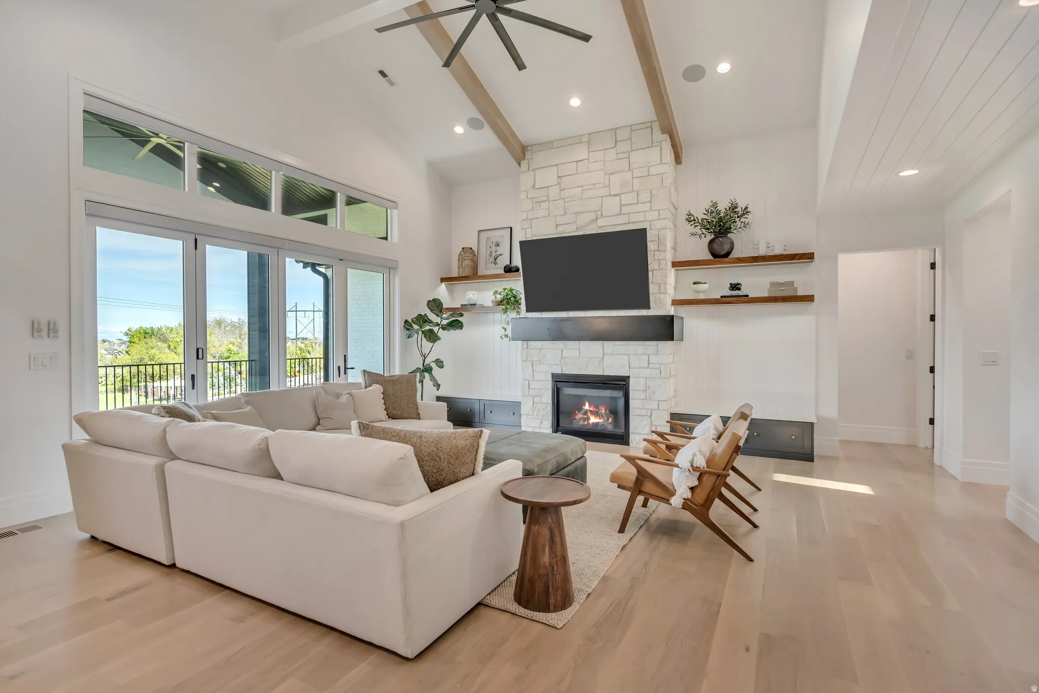 Living room with a stone fireplace, light wood-style flooring, a ceiling fan, recessed lighting, and lofted ceiling