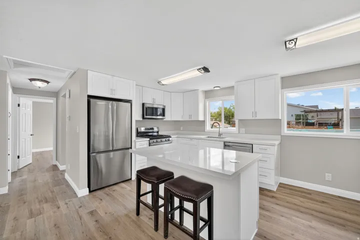 Kitchen featuring stainless steel appliances, a kitchen breakfast bar, white cabinets, and light wood-style flooring