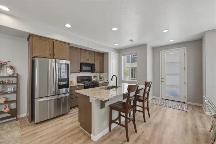 Kitchen with black appliances, light stone countertops, a breakfast bar, a center island with sink, and recessed lighting
