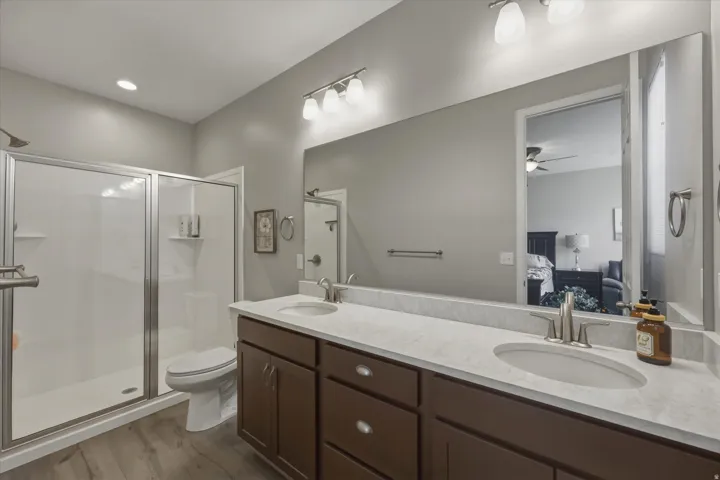 Full bath featuring connected bathroom, double vanity, a shower stall, and dark wood finished floors