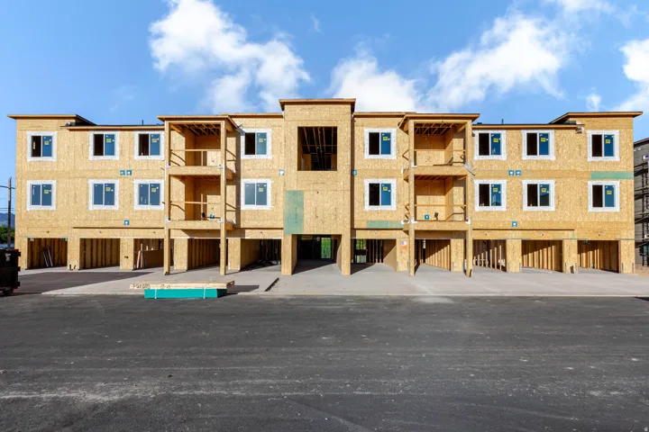 Multi-story building under construction, featuring multiple window openings, tiered balcony framing, and an integrated ground-level parking area