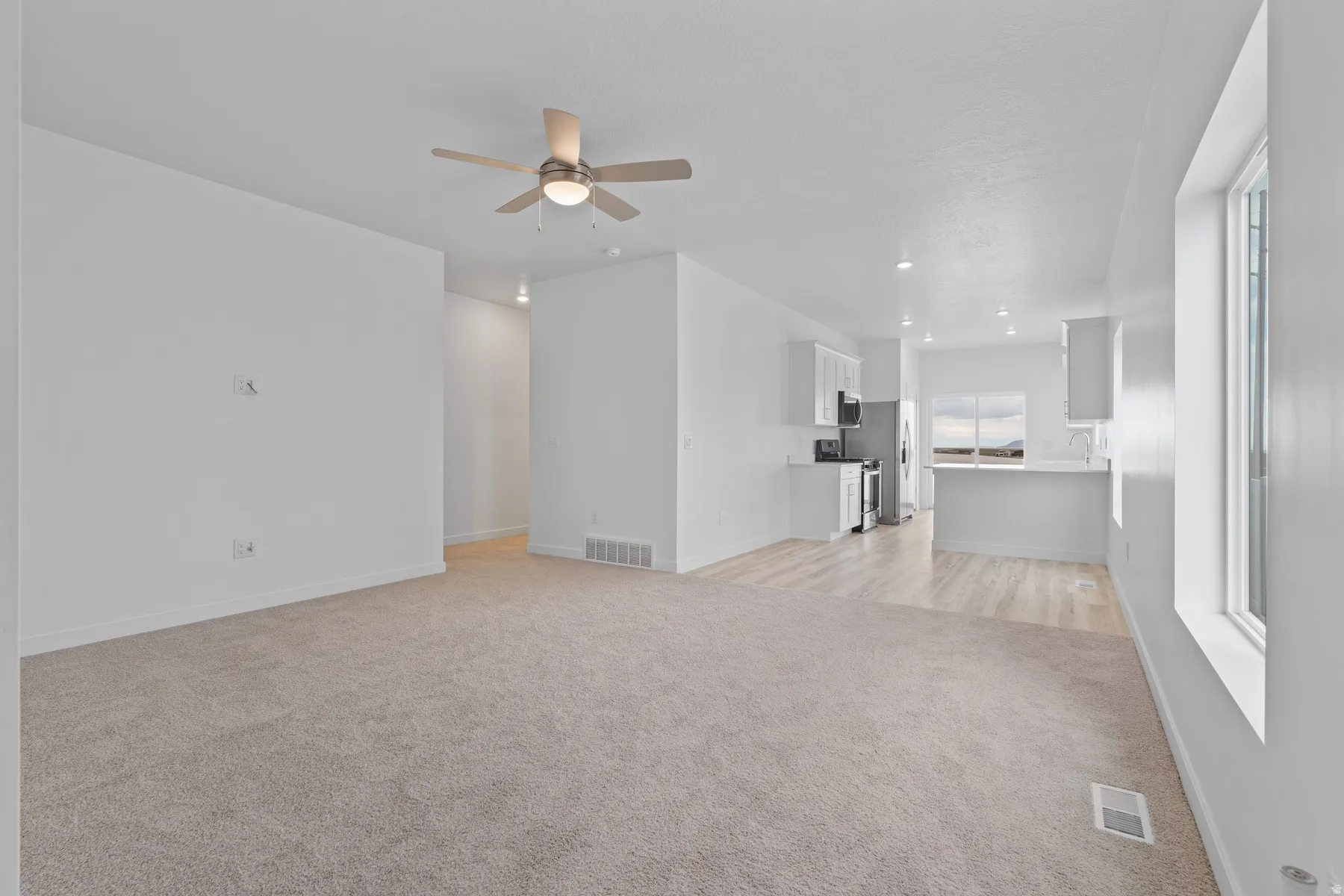 Open-concept living area featuring light-colored carpeting, a ceiling fan, and recessed lighting