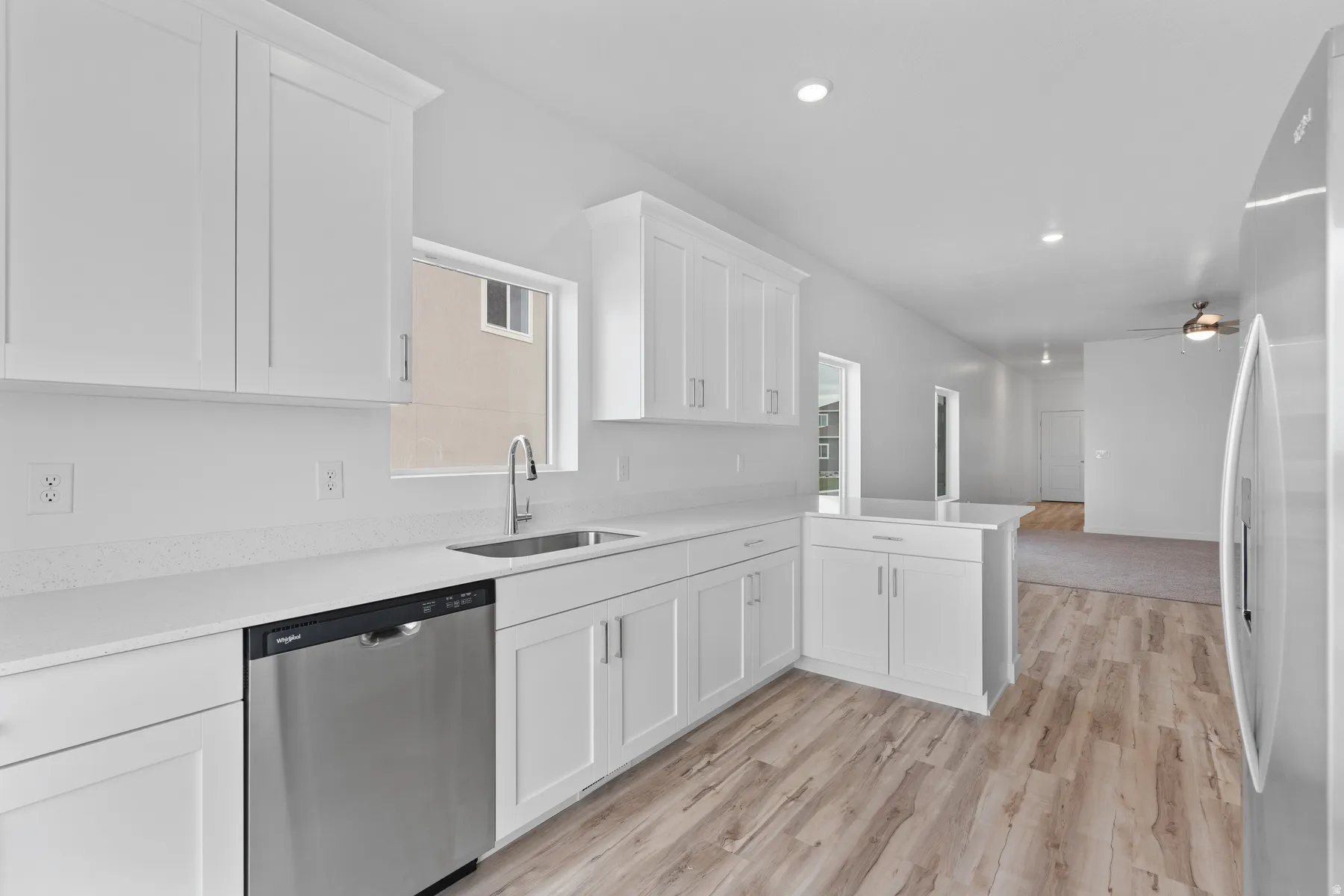 Kitchen featuring white cabinetry, light-toned countertops, a stainless steel sink with a gooseneck faucet, a stainless steel dishwasher, and wood-finish flooring