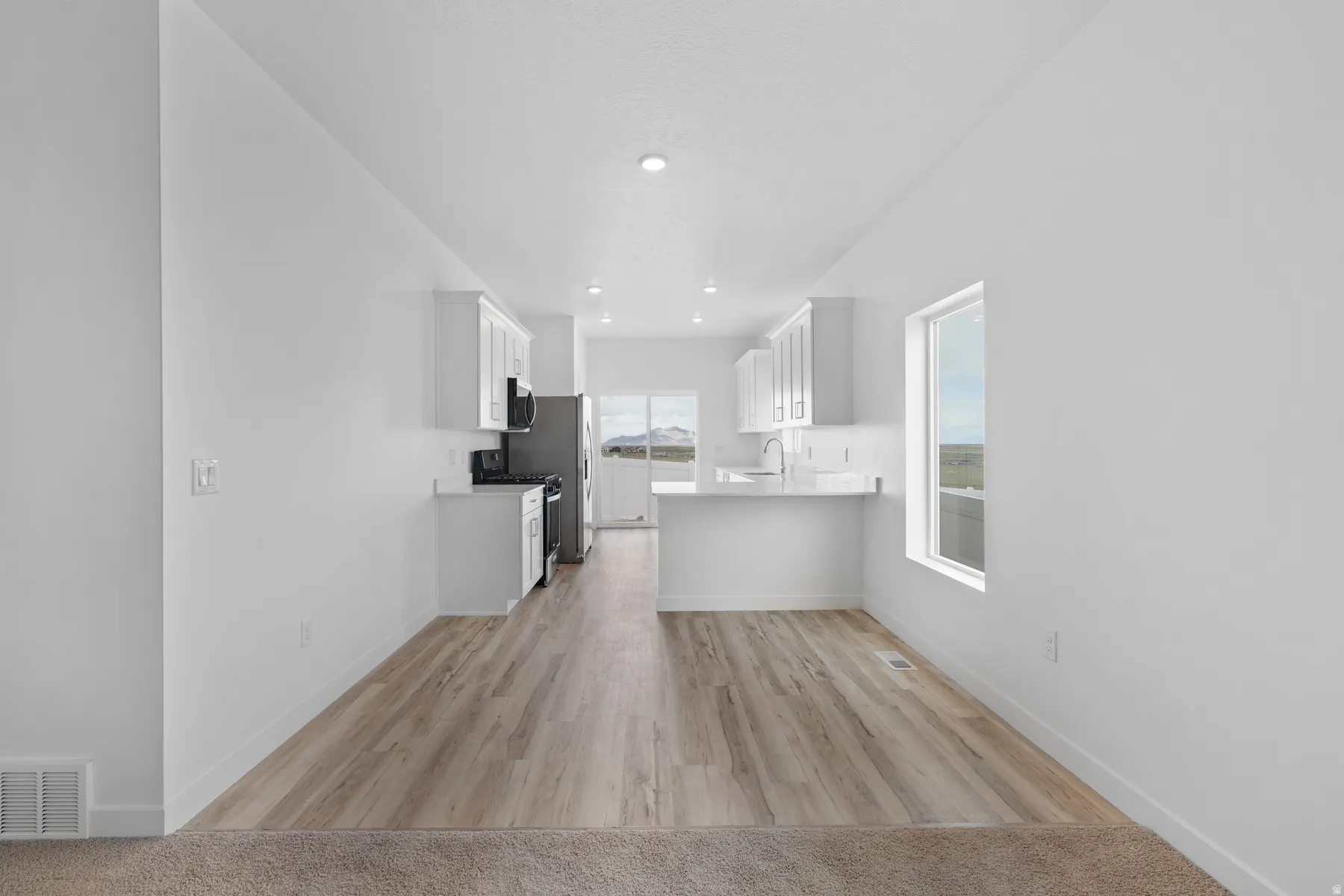Open-concept kitchen and dining area featuring wood-finish flooring, white cabinetry, a built-in kitchen island, recessed lighting, and a large window