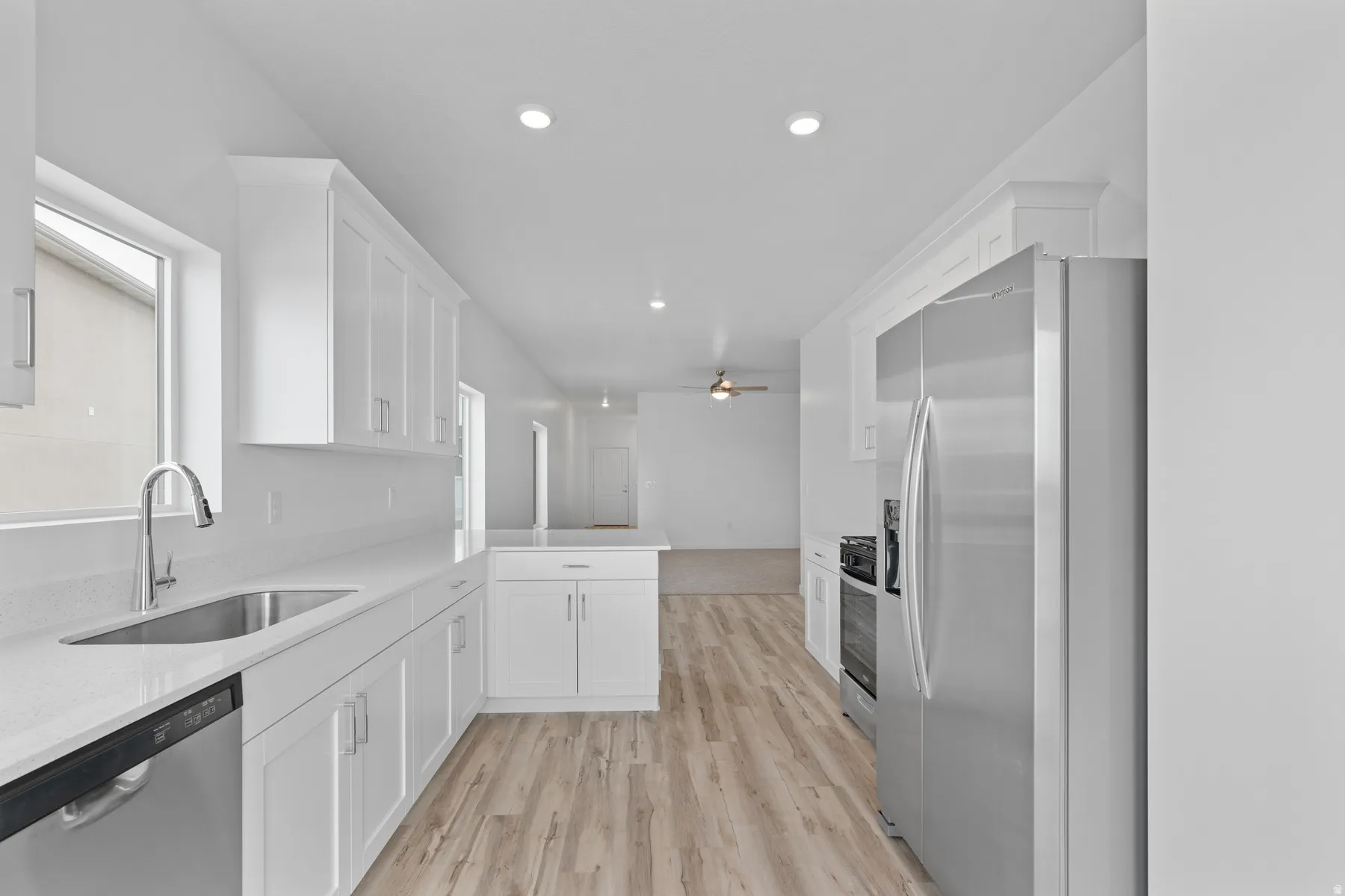 Kitchen featuring white shaker cabinetry, stainless steel appliances, a stainless steel sink with a gooseneck faucet, light-toned wood-finish flooring, and recessed lighting