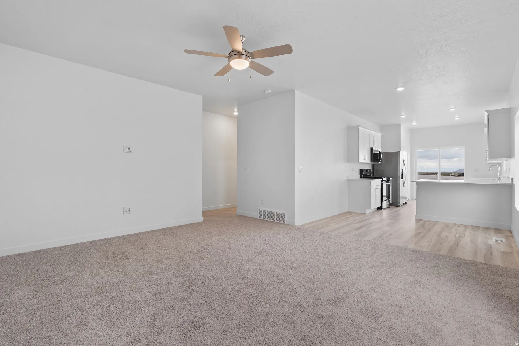 Open-concept living area featuring a ceiling fan, plush carpet flooring, recessed lighting, and light wood-finish flooring extending into the kitchen