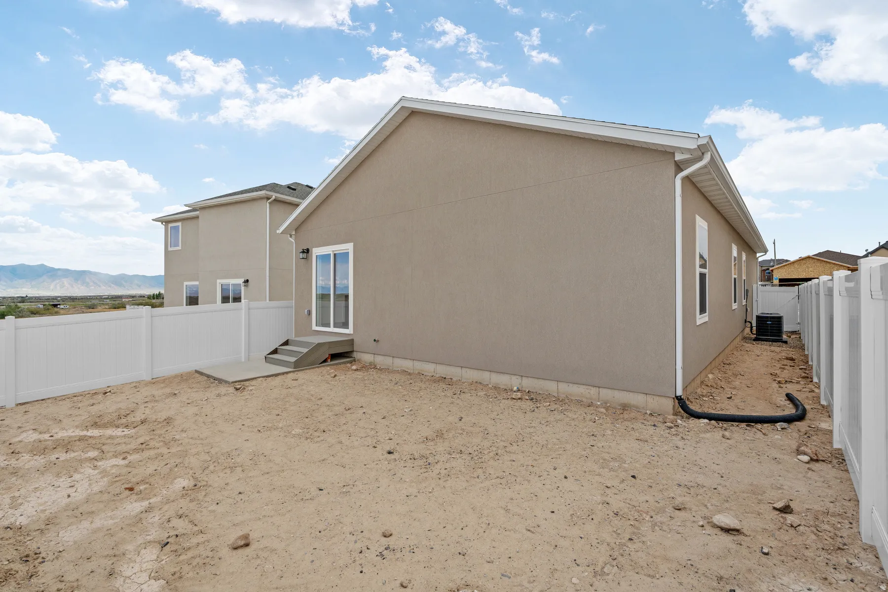 Rear exterior featuring stucco siding, white vinyl fencing, concrete patio, and sliding glass door access