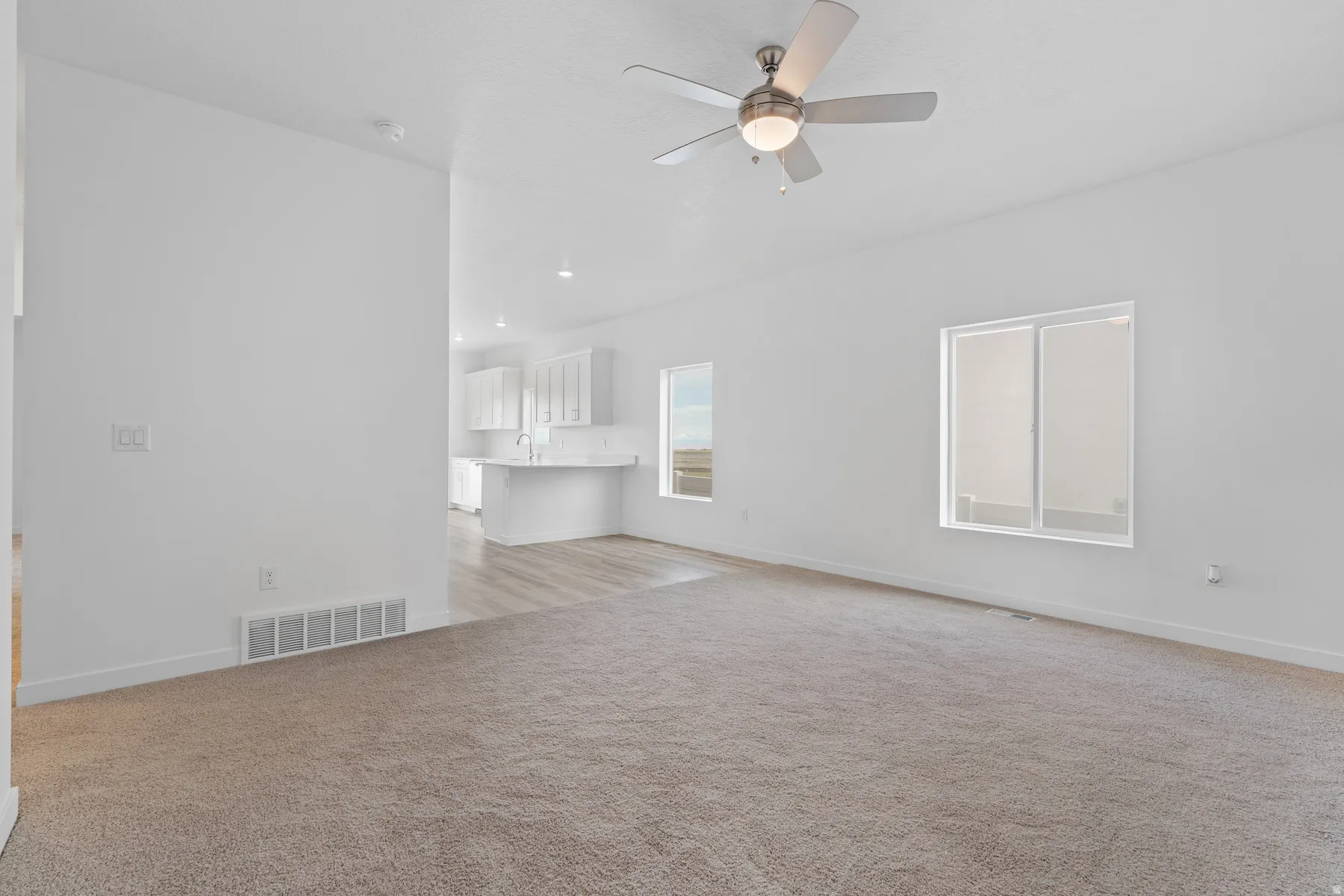 Open-concept living area with neutral carpeting and a ceiling fan