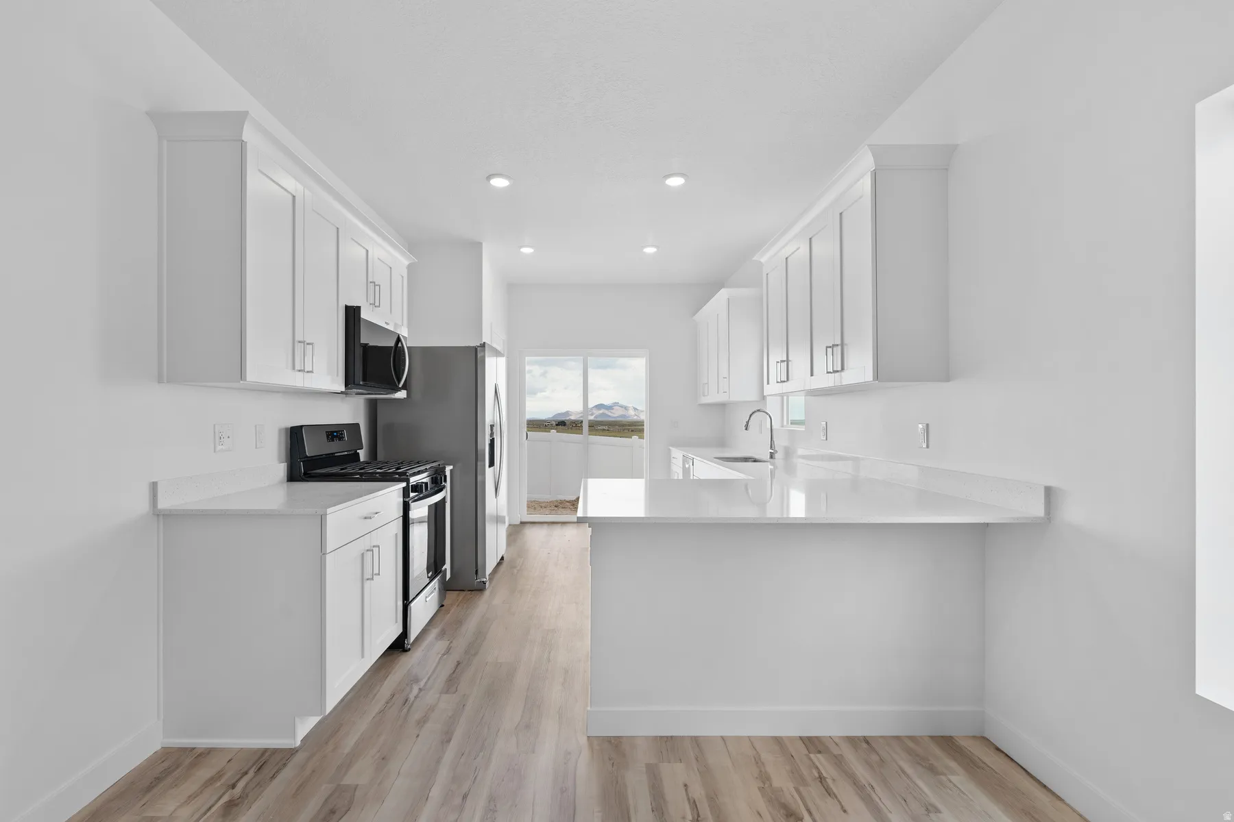 Bright kitchen featuring white shaker cabinetry, stainless steel appliances, quartz countertops, a double basin sink with a gooseneck faucet, and wood-finish flooring