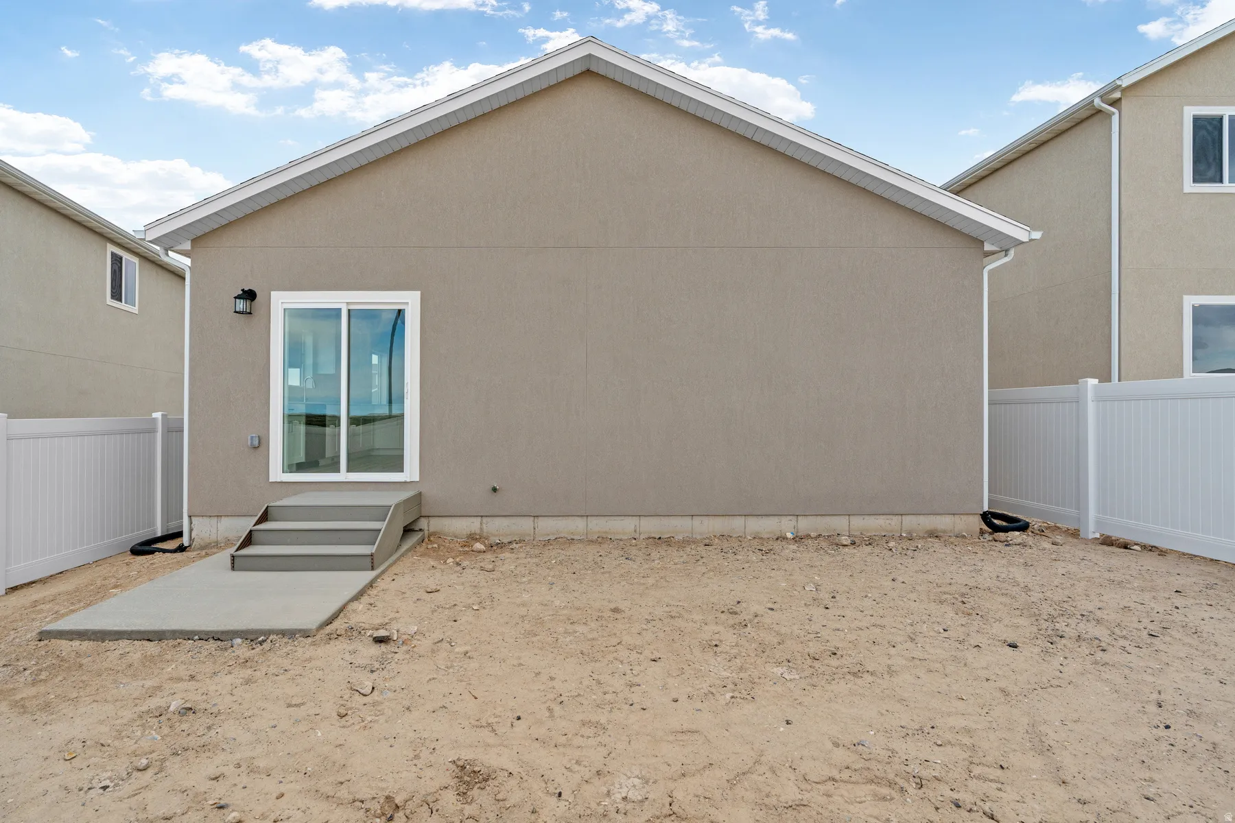 Rear exterior featuring stucco siding, white vinyl fencing, a concrete patio, and a sliding glass door