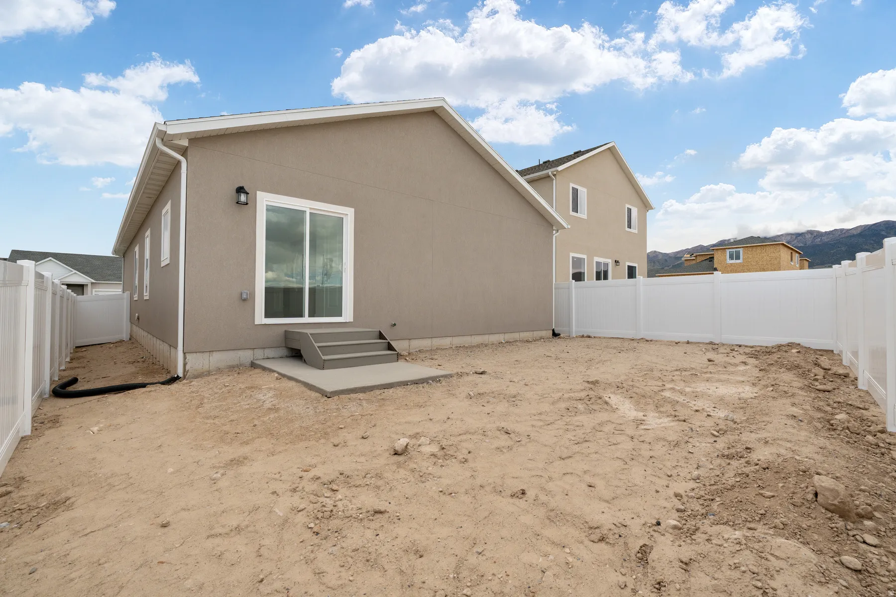 Rear exterior featuring neutral stucco siding, white vinyl fencing, a sliding glass door, and a concrete patio with steps