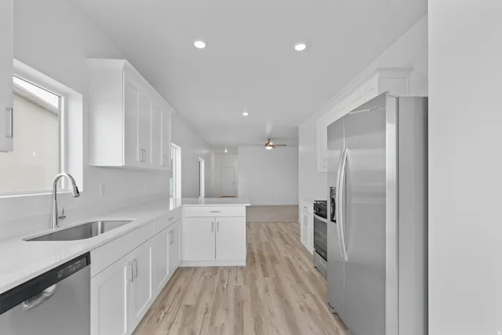Kitchen featuring white shaker cabinetry, stainless steel appliances, a stainless steel sink with a gooseneck faucet, light-toned wood-finish flooring, and recessed lighting
