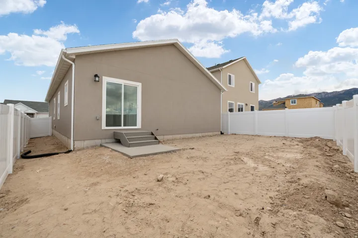 Rear exterior featuring neutral stucco siding, white vinyl fencing, a sliding glass door, and a concrete patio with steps