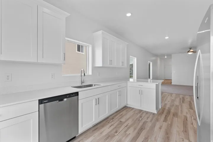 Kitchen featuring white cabinetry, light-toned countertops, a stainless steel sink with a gooseneck faucet, a stainless steel dishwasher, and wood-finish flooring