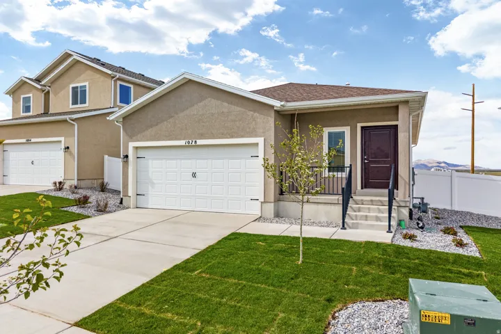 Stucco exterior featuring a single-car garage, concrete driveway, and a front entry with dark brown door and black railing