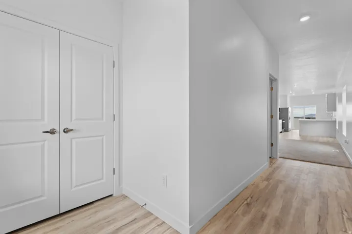 Interior hallway featuring wood-finish flooring, white baseboards, and a pair of paneled doors with brushed nickel hardware