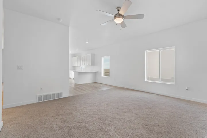 Open-concept living area with neutral carpeting and a ceiling fan