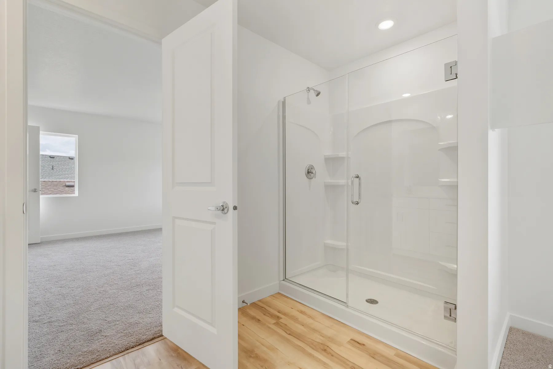 Enclosed shower with clear glass door, chrome fixtures, and built-in shelving