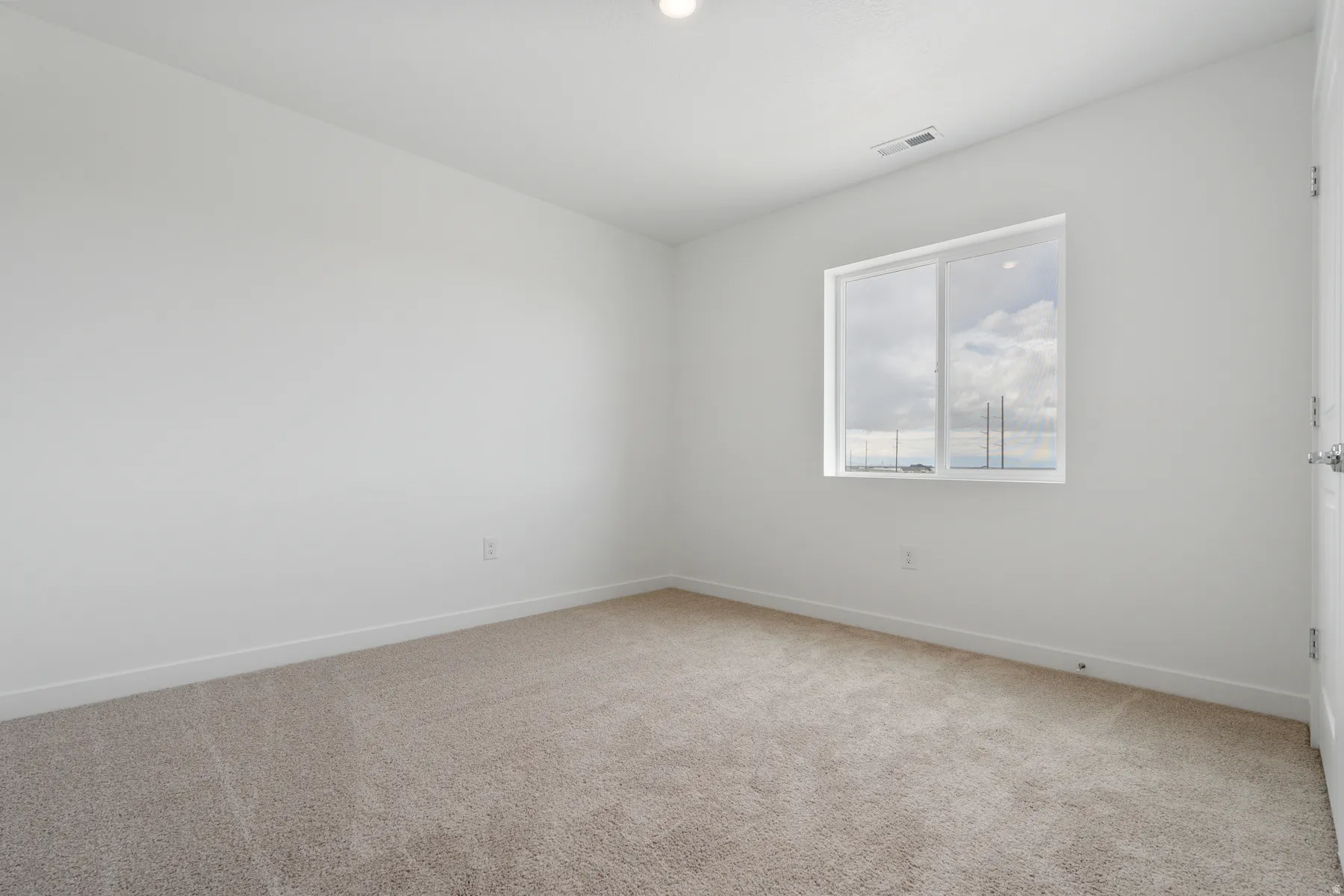 Neutral wall tones, window, white trim, light-toned carpeting, and a ceiling light fixture