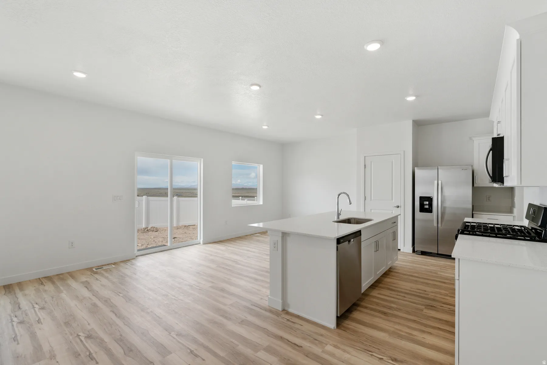 Open-concept living space featuring wood-finish flooring, recessed lighting, and a kitchen island with an integrated sink