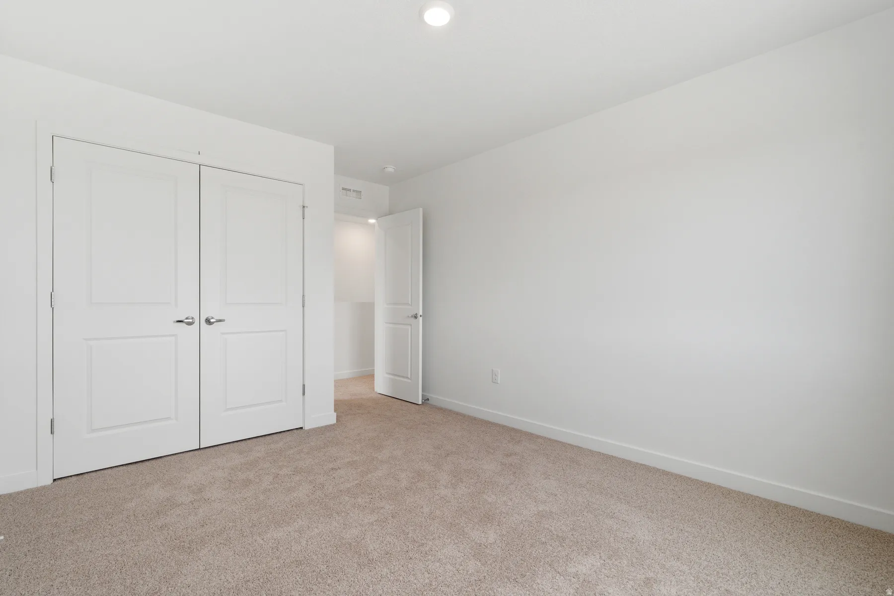 Carpeted room featuring white walls, a single recessed ceiling light, and a double-door closet with polished chrome hardware