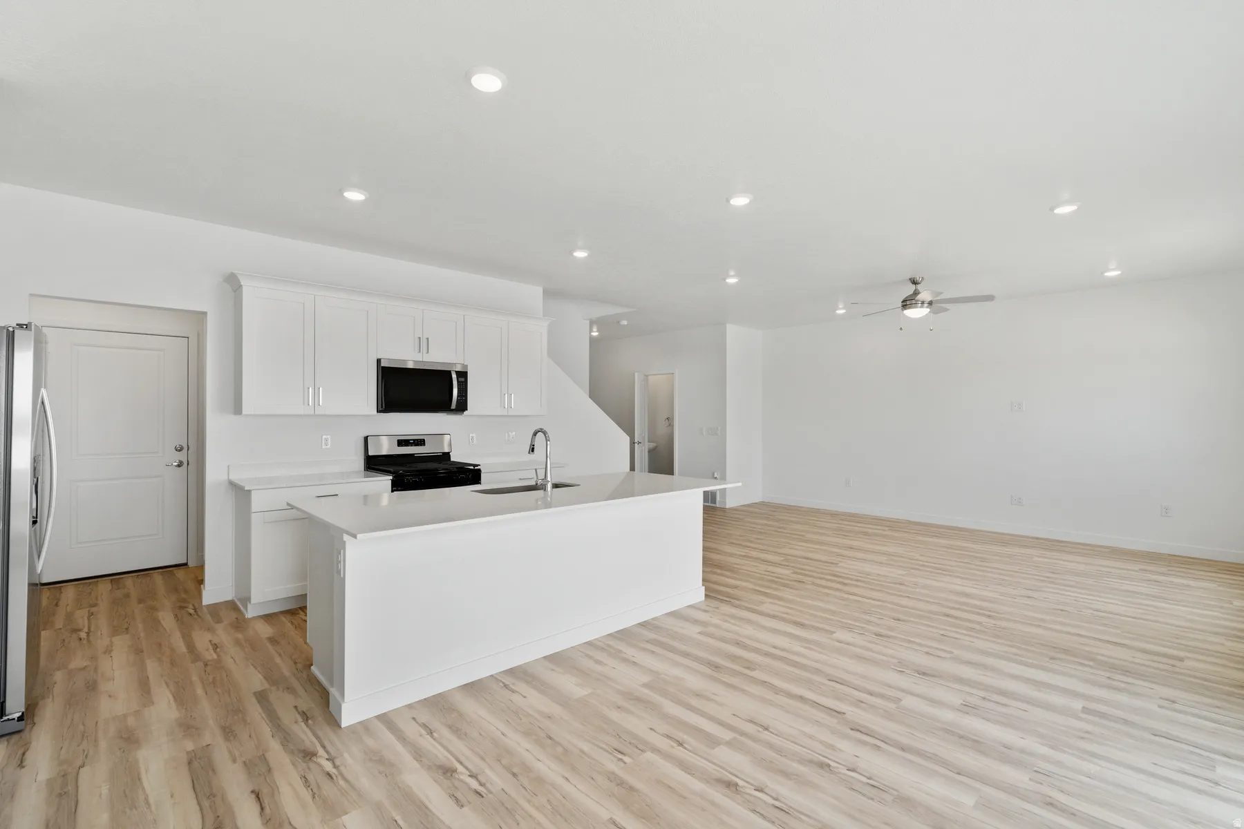 Open-concept living area featuring light wood-finish flooring, recessed lighting, and a modern ceiling fan