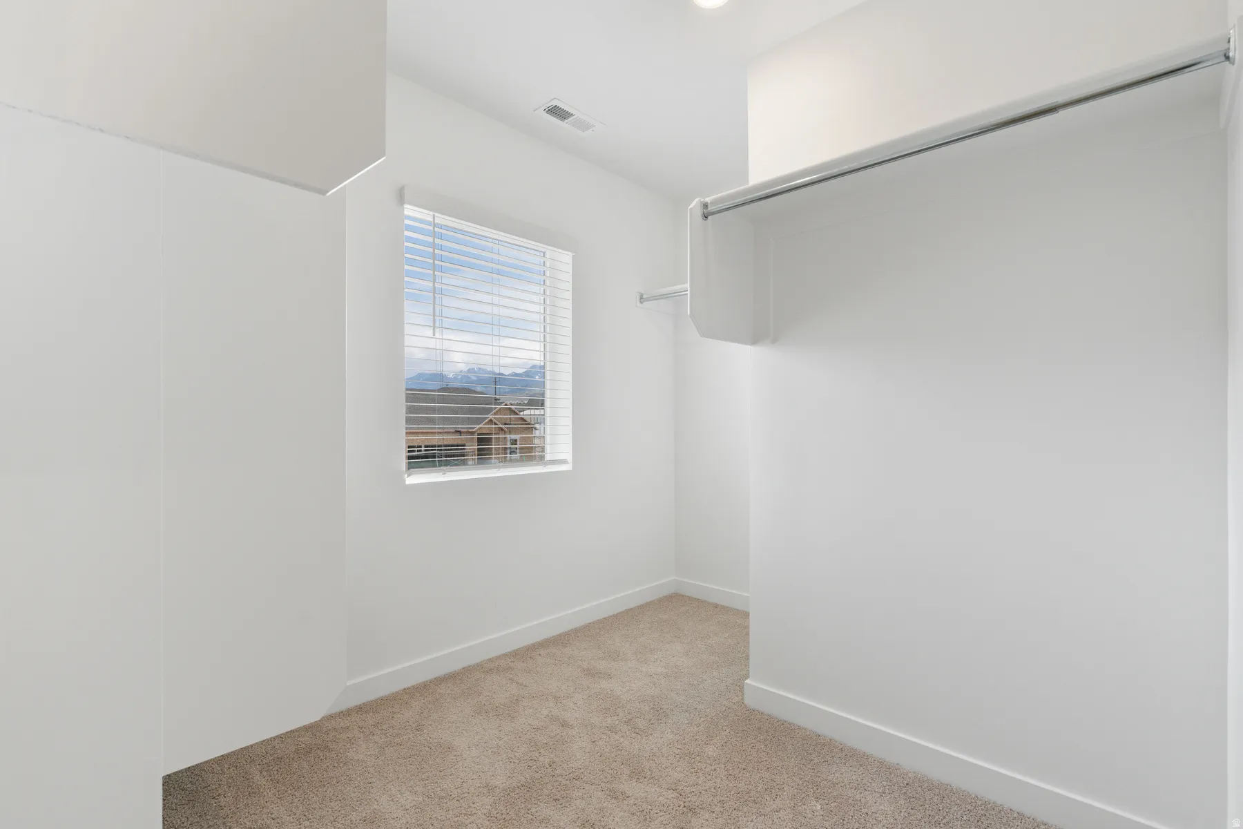 Walk-in closet featuring plush carpet flooring, white walls, and a window with horizontal blinds