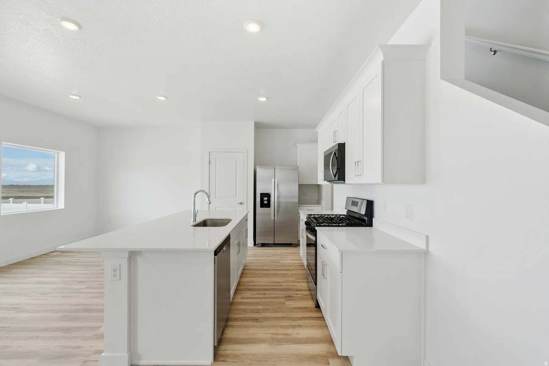 Bright kitchen featuring white cabinetry, stainless steel appliances, a white countertop island with an undermount sink, recessed lighting, and wood-finish flooring