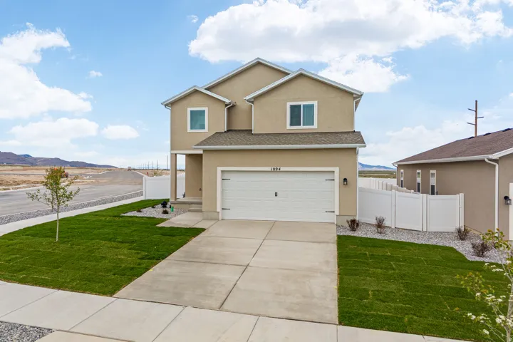 Two-story stucco residence with a two-car garage, concrete driveway, and front sidewalk