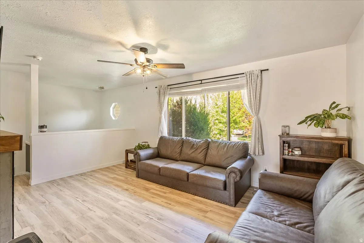 Living area featuring a textured ceiling, light wood-type flooring, and ceiling fan