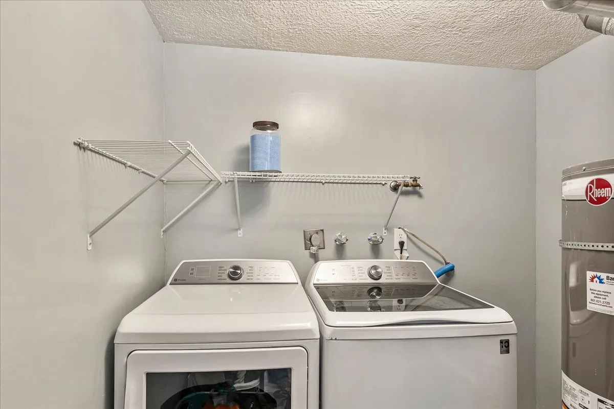 Laundry room with electric water heater, a textured ceiling, and independent washer and dryer