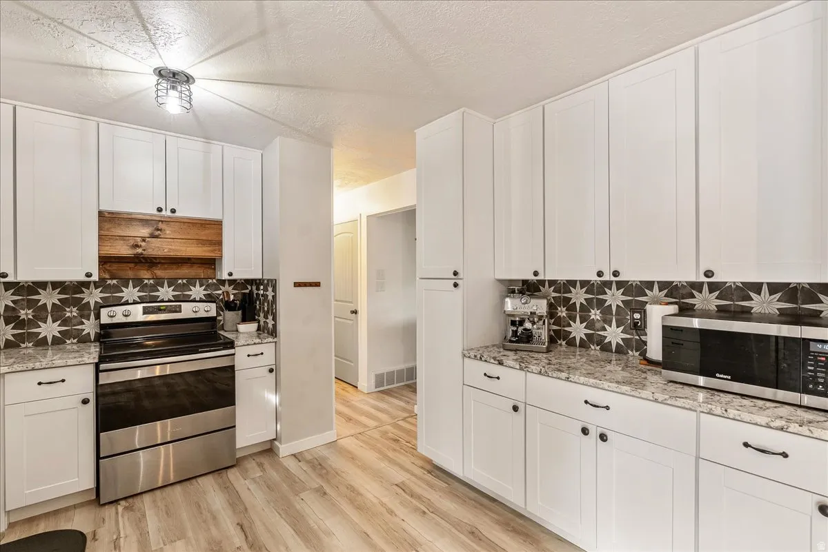 Kitchen featuring stainless steel appliances, white cabinetry, tasteful backsplash, light stone counters, and a textured ceiling