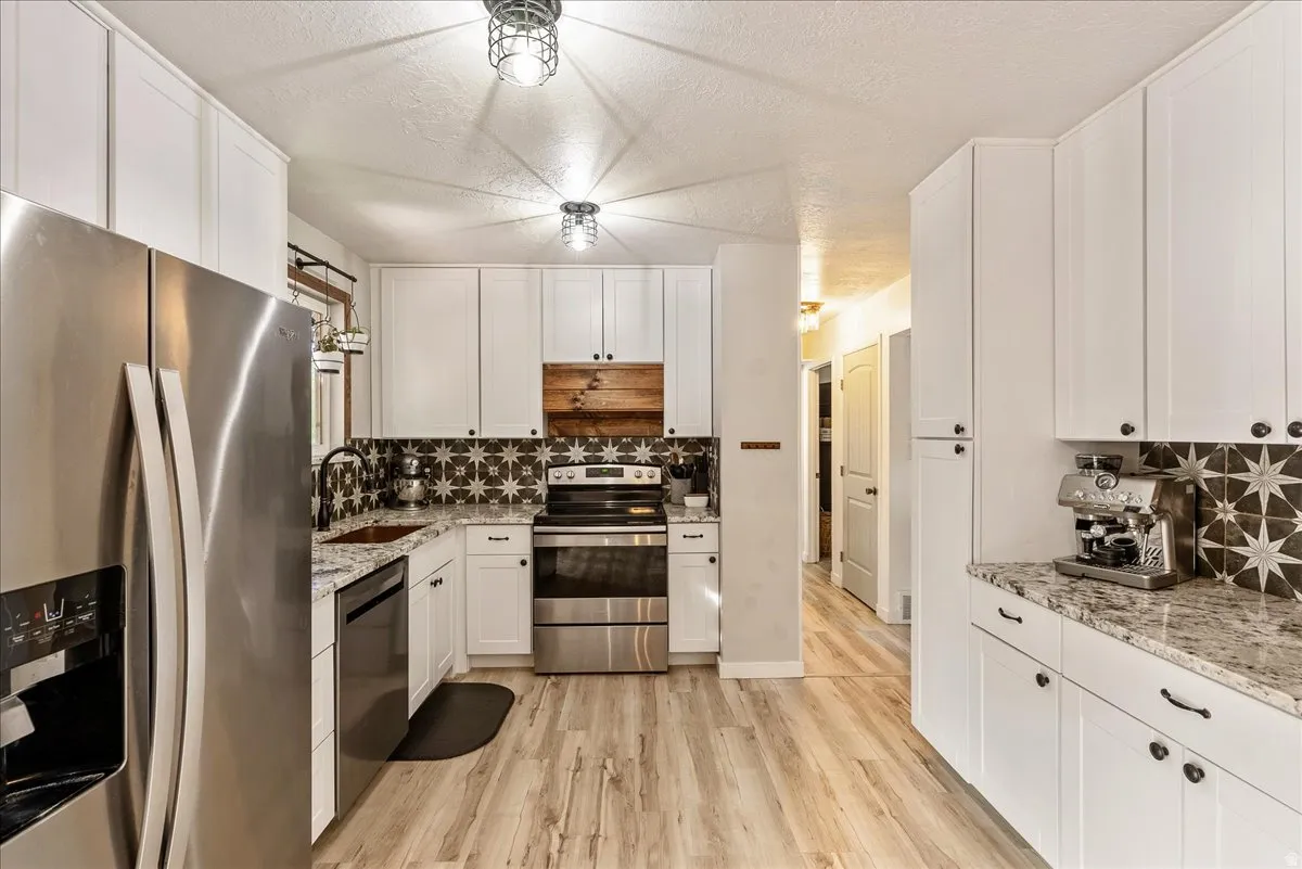 Kitchen with stainless steel appliances, white cabinets, light stone countertops, a textured ceiling, and light wood-type flooring