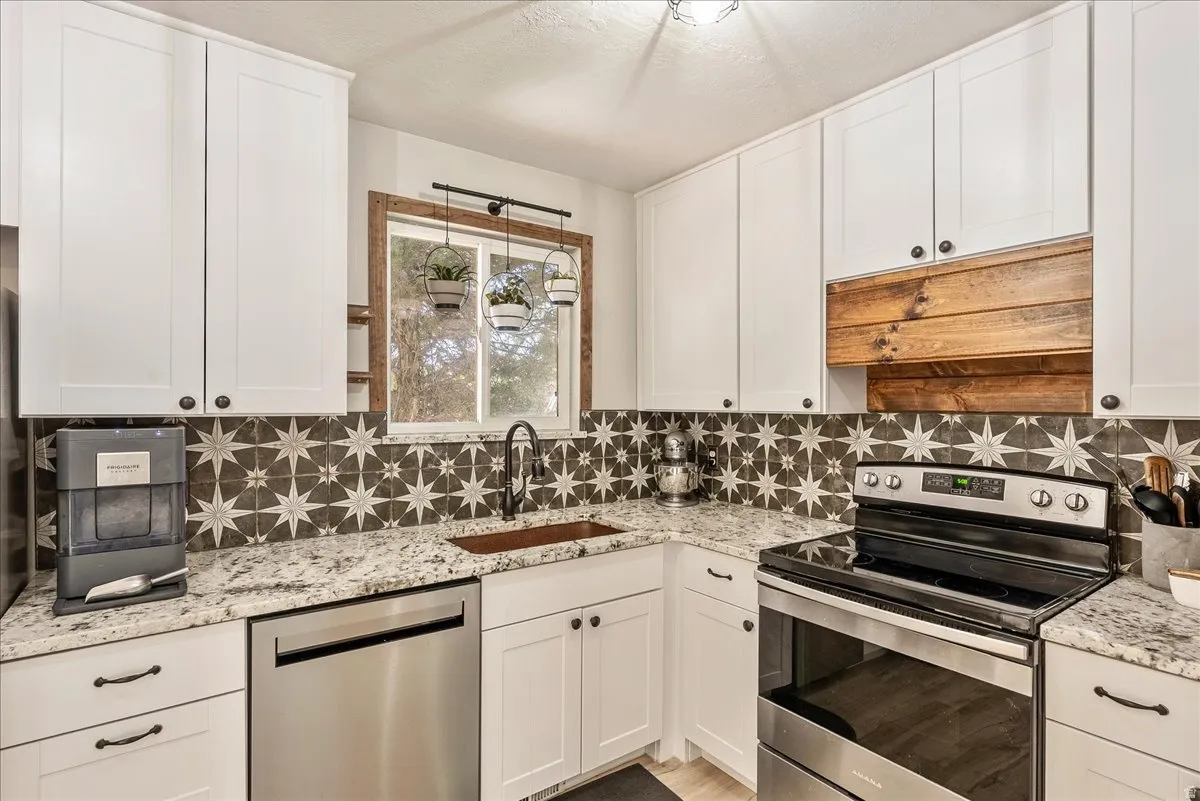 Kitchen featuring stainless steel appliances, white cabinetry, light stone countertops, and backsplash