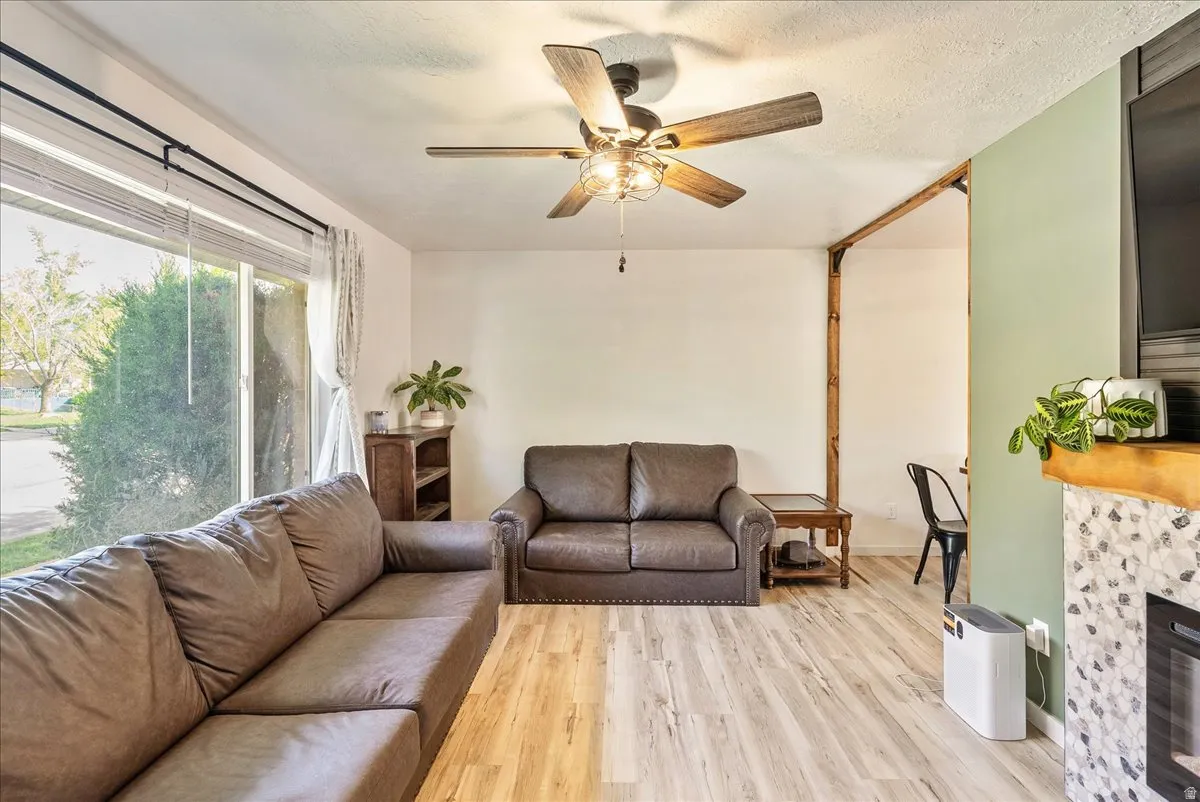 Living area featuring light wood-style floors, a fireplace, ceiling fan, and a textured ceiling