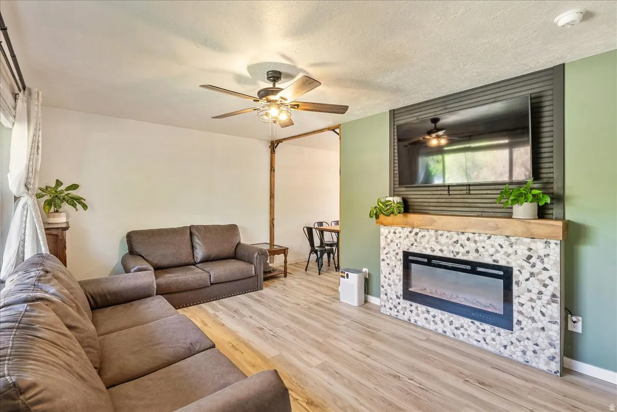Living room featuring light wood-type flooring, a tiled fireplace, ceiling fan, and a textured ceiling