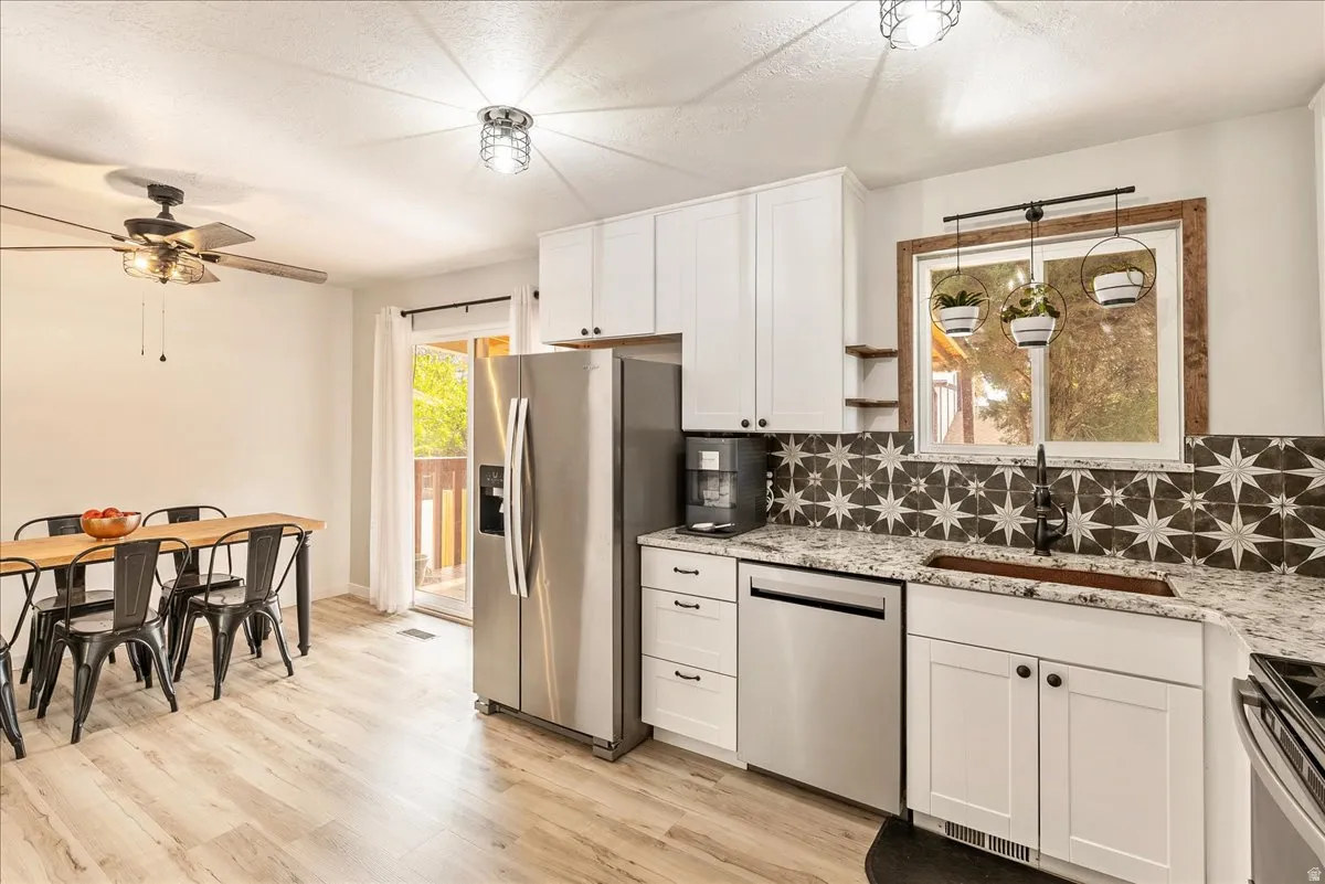 Kitchen featuring white cabinetry, stainless steel appliances, backsplash, light wood finished floors, and light stone counters