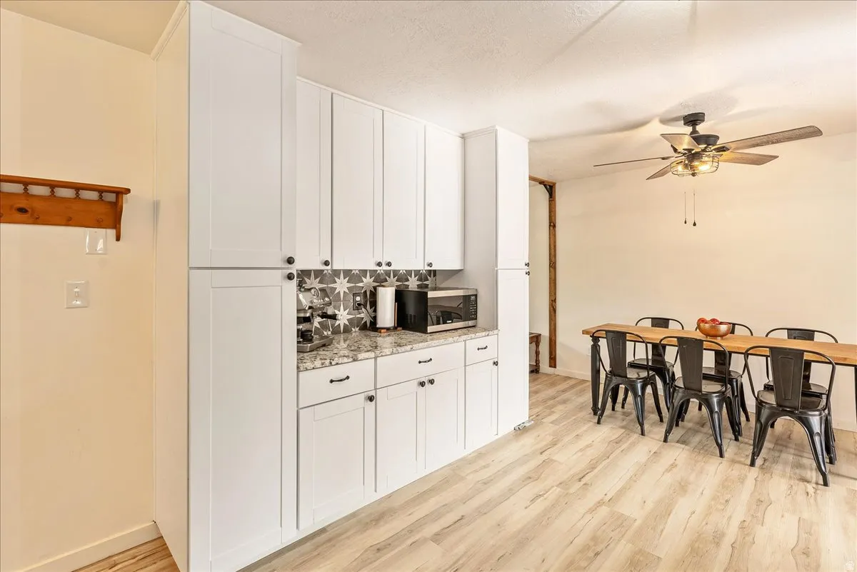 Kitchen with light wood-style flooring, stainless steel microwave, white cabinets, a ceiling fan, and a textured ceiling