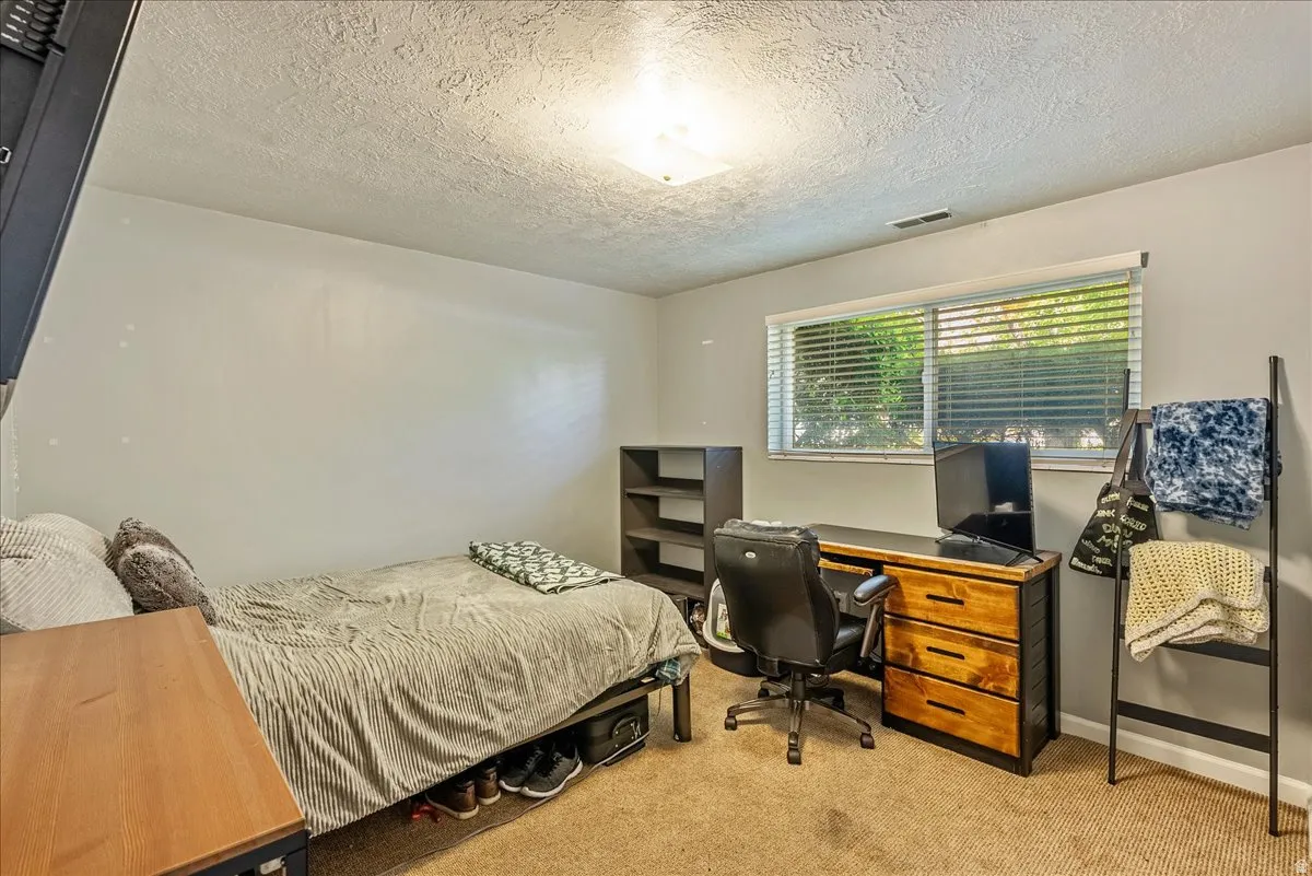 Bedroom featuring a textured ceiling, light carpet, and a desk
