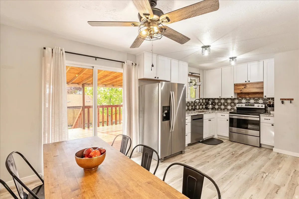 Kitchen featuring stainless steel appliances, light wood-style flooring, white cabinets, backsplash, and ceiling fan