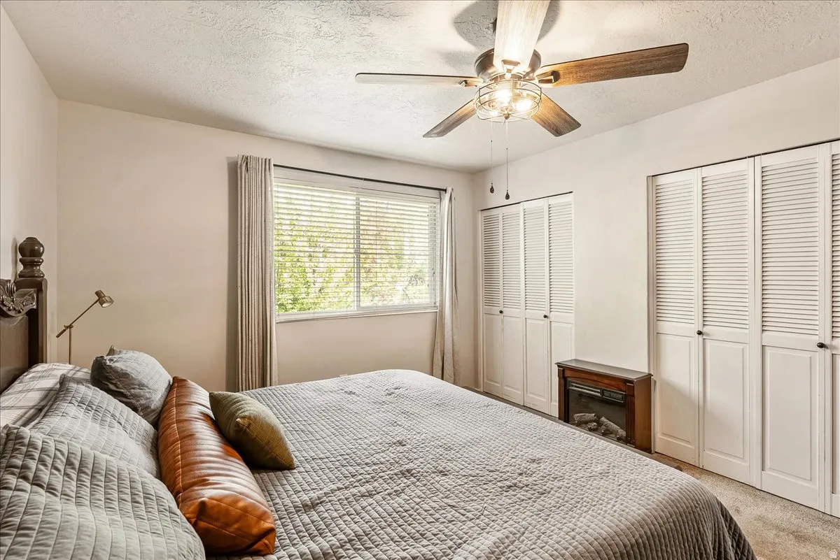 Carpeted bedroom with two closets, a textured ceiling, and ceiling fan